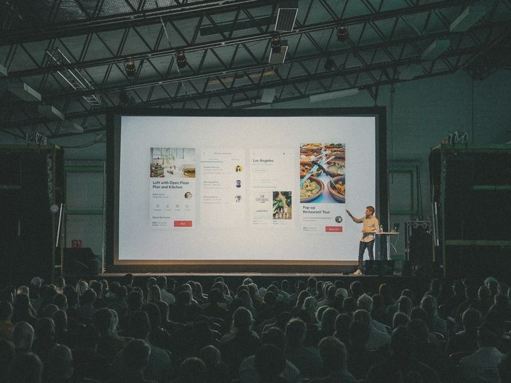 A presenter shows a product on a big screen to a full room