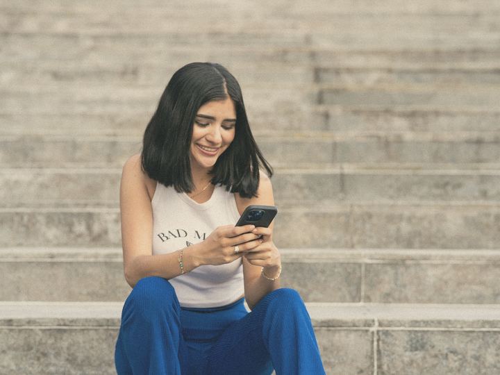A woman smiles at her phone on city steps